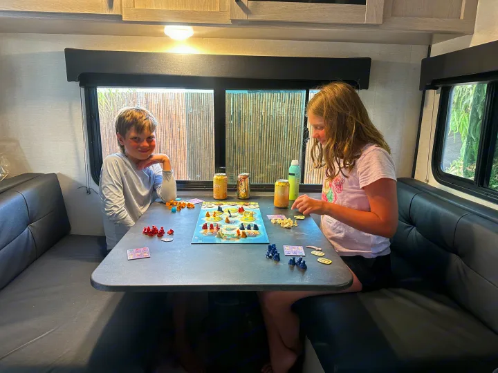 Two kids enjoy a board game at a dinette inside a cozy RV rental, perfect for family travel.. Coachmen Apex Nano - Off Grid 2022
