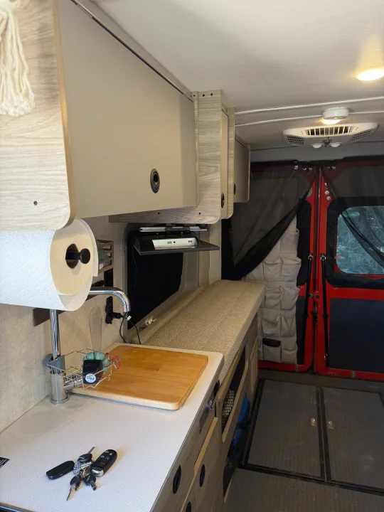 RV rental interior featuring a compact kitchen with sink, paper towels, overhead cabinets, and a comfortable bench/bed.. Winnebago Solis 2024
