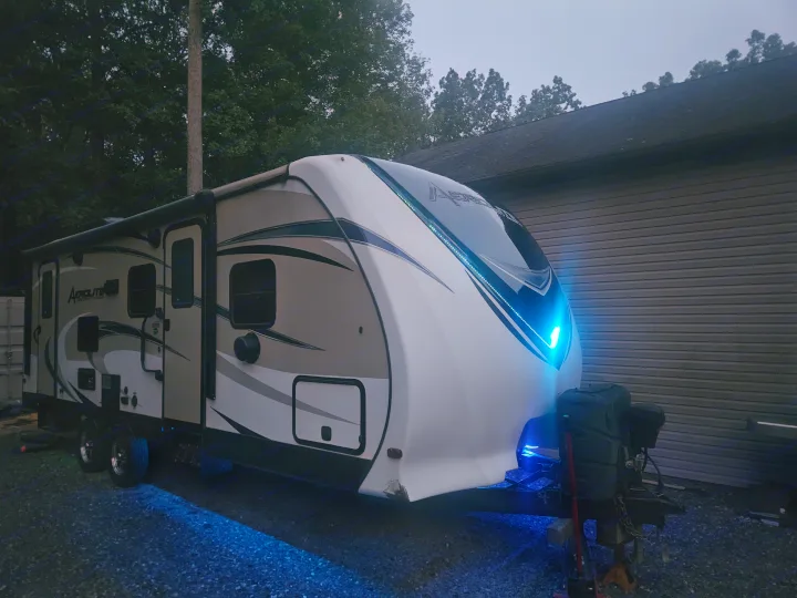 A modern Aerolite travel trailer, showcasing its bright blue LED lighting at night, parked on gravel. Ideal for RV rental.. Dutchmen 242bhsl 2017