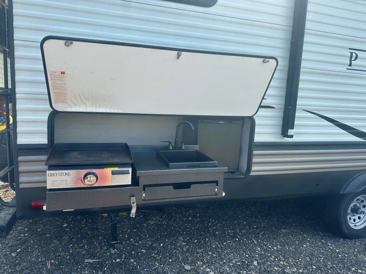 This RV rental features a convenient outdoor kitchen with a griddle, sink, and fridge, perfect for camping.. Forest River Palomino Puma 2022