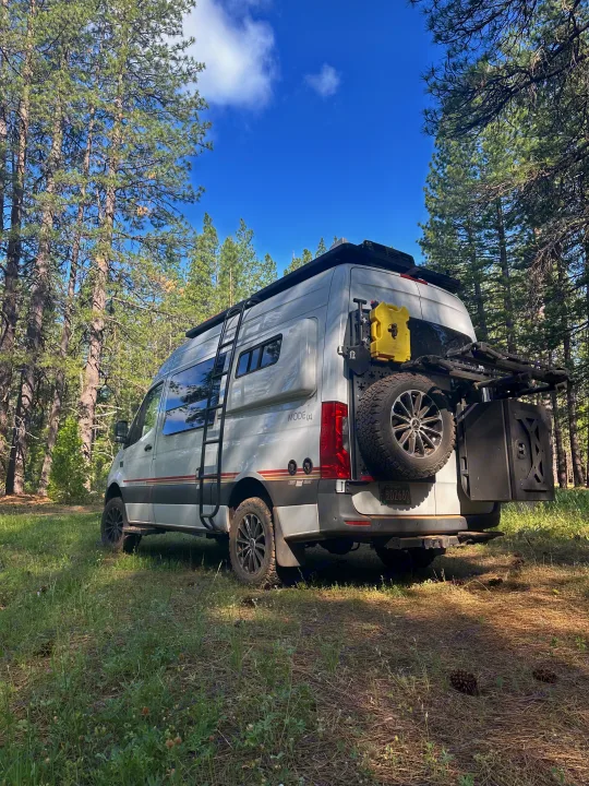 White Sprinter camper van, an ultimate RV rental for forest adventures, parked under blue skies.. Storyteller Overland Storyteller Overland Class B 2021