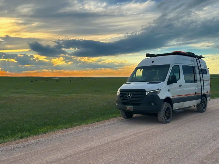 White Mercedes Sprinter RV rental on a dirt road at sunset. Explore vast green plains with distant bison from your van.. Storyteller Overland Storyteller Overland Class B 2021