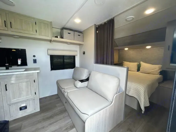 Clean RV rental interior featuring a bright living area with sofa, kitchenette, and a private bed. Perfect for your next trip.. Coachman RV 261BH 2025