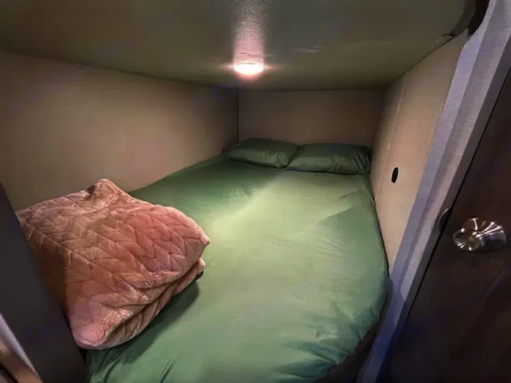 Cozy, compact bunk bed in an RV rental, featuring green bedding and a soft blanket under an overhead light.. Coachman RV 261BH 2025