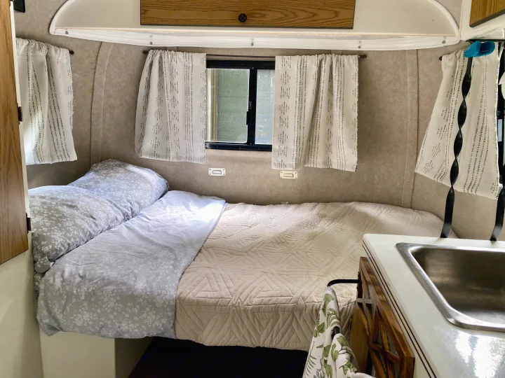 Cozy rv rental interior: comfortable bed with floral and quilted bedding, windows with curtains, and a compact sink.. Scamp Scamp Trailer 1999