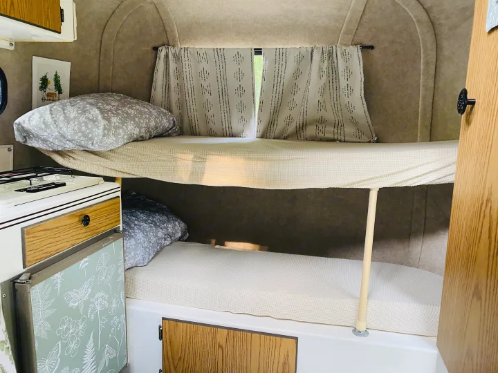 Compact RV rental interior featuring cozy bunk beds, a Dometic fridge, and window curtains.. Scamp Scamp Trailer 1999