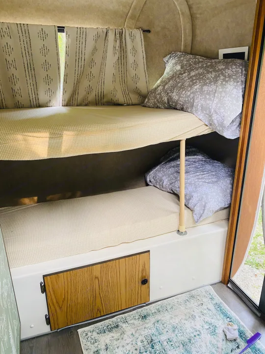 Bunk beds inside an RV rental, offering a cozy sleep space with floral pillows & patterned curtains.. Scamp Scamp Trailer 1999