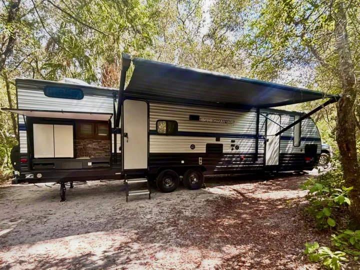 RV rental: A Grey Wolf travel trailer with extended awning and outdoor kitchen set up on sandy ground at a sunny, wooded campsite.. Forest River Cherokee Grey Wolf 2019