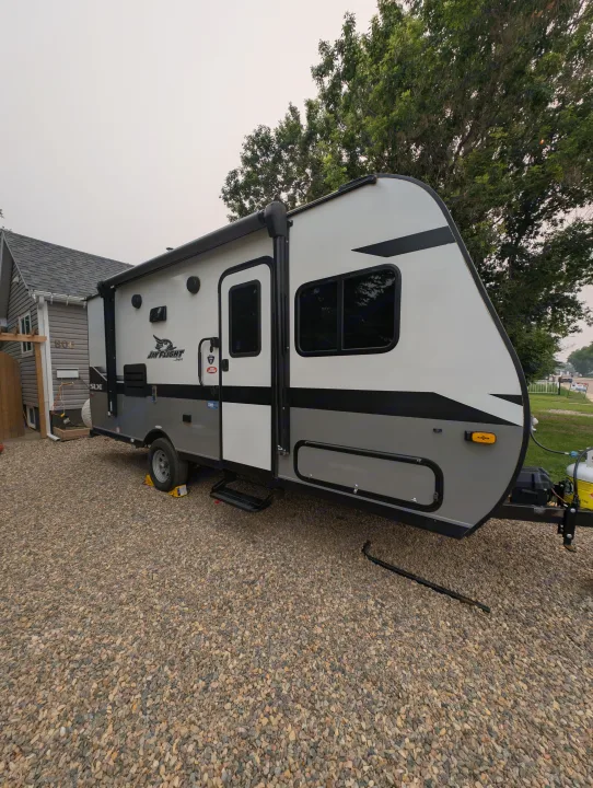 This white and gray RV (Jayco travel trailer), ideal for an RV rental, is parked on a gravel driveway.. Jayco Jay Flight SLX 2022