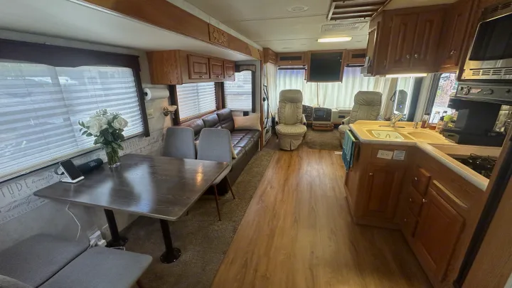 Well-appointed RV rental interior showing a dining table with flowers, cozy couch, kitchen, and the driver's cockpit.. Holiday Rambler Vacationer 2003