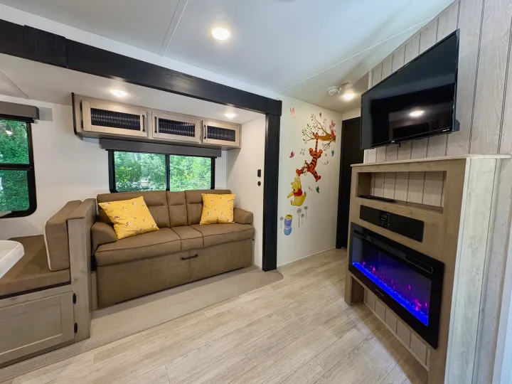 Bright RV rental interior with a comfy sofa, entertainment system, electric fireplace, and fun Pooh wall art.. Forest River Puma 2026