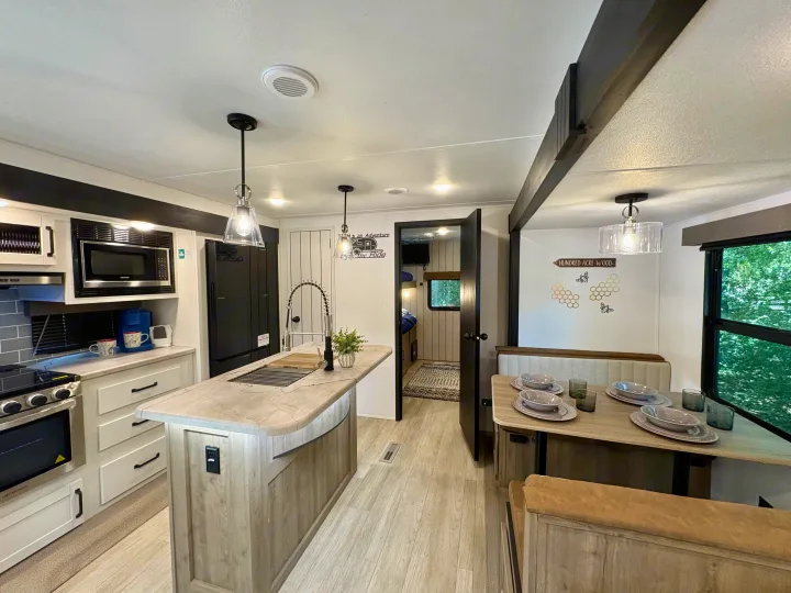 Modern RV rental interior with a light-filled kitchen, central island, dining booth, and a glimpse into a bunk room.. Forest River Puma 2026