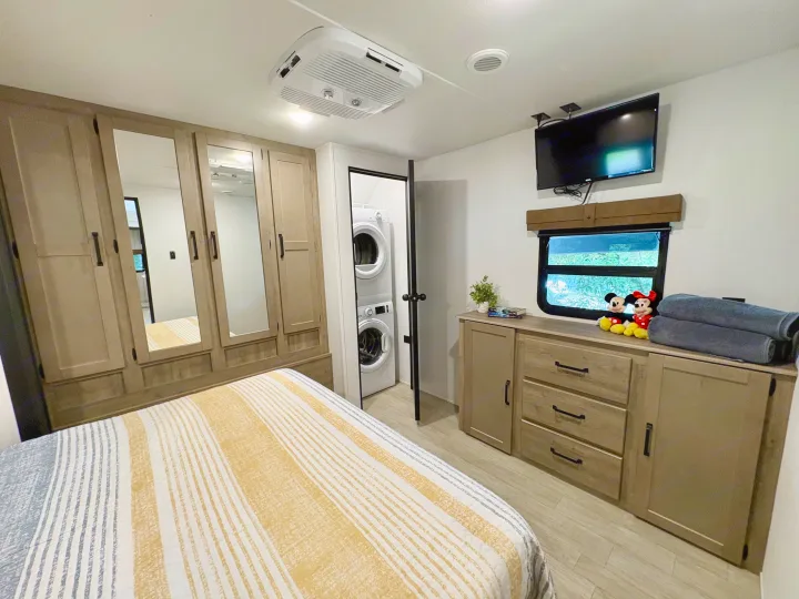 Bright RV rental bedroom with a striped bed, stacked washer/dryer, TV, and ample storage for comfortable travel.. Forest River Puma 2026