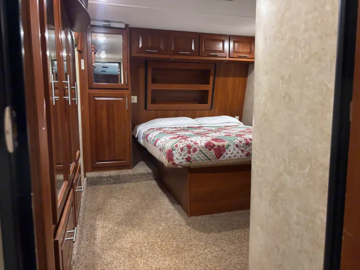 Cozy RV rental bedroom featuring a comfortable bed with floral quilt, ample built-in storage cabinets, and carpeted flooring.. Keystone Fuzion 2015