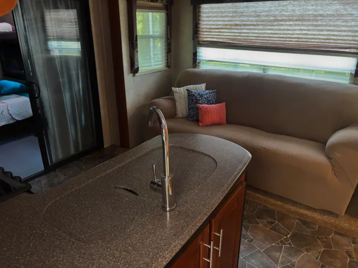 Cozy RV rental living area with a kitchen counter, sink, comfortable sofa, and windows. Ideal for travel!. Keystone Fuzion 2015