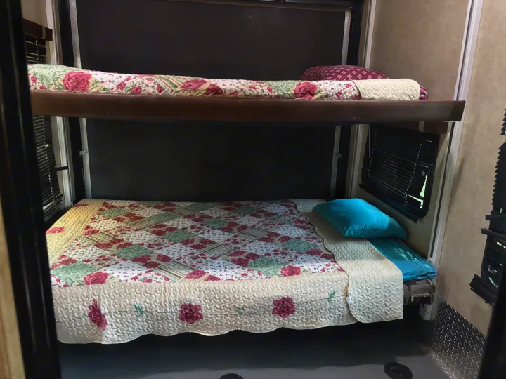 Spacious RV rental bunk beds with colorful floral quilts & cozy pillows, perfect for travel.. Keystone Fuzion 2015