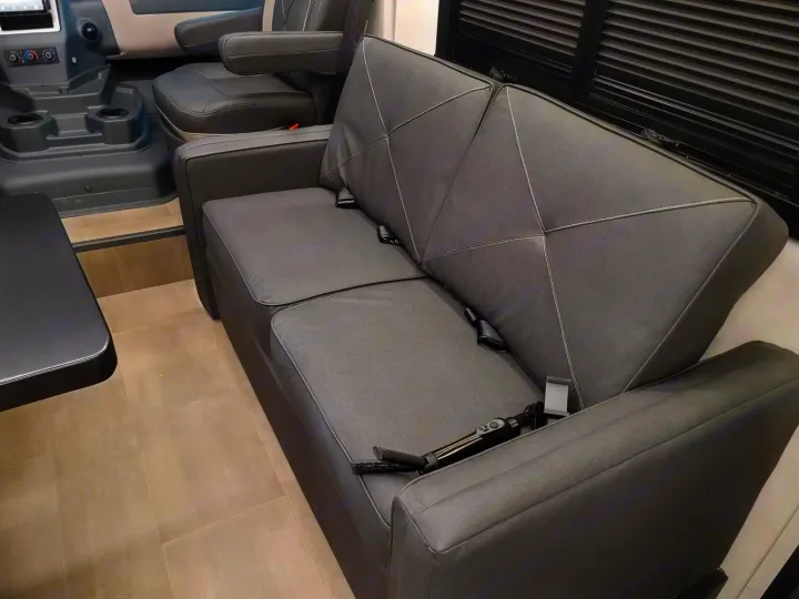 Clean, modern RV rental interior: grey sofa with seatbelts, black side table, and a glimpse of the front cabin.. Coachmen Euro 2025