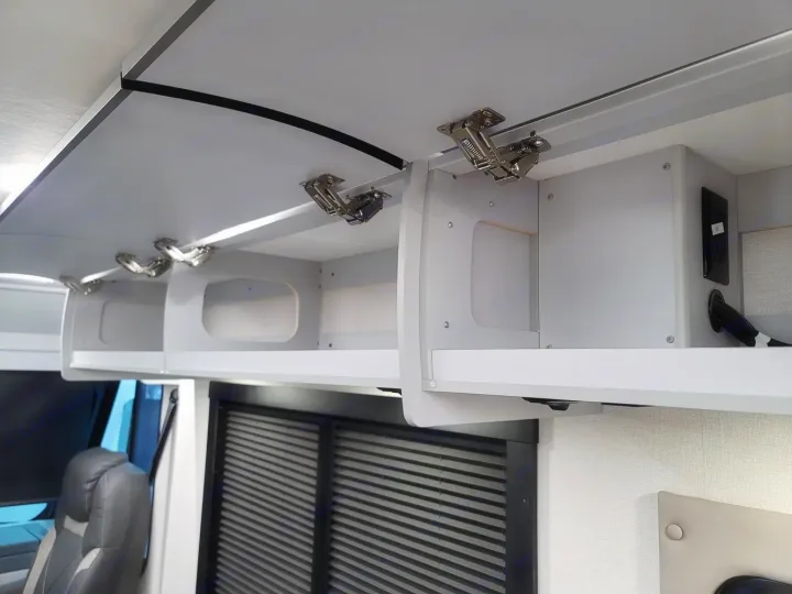 Inside an RV rental: Open overhead cabinets with visible hinges and storage spaces. Power outlets are seen on the right.. Coachmen Euro 2025