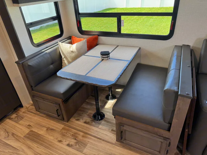 RV rental dinette: dark gray benches, light table, and windows framing green outdoor scenery. Ideal for travelers.. SportTrek Venture 2024