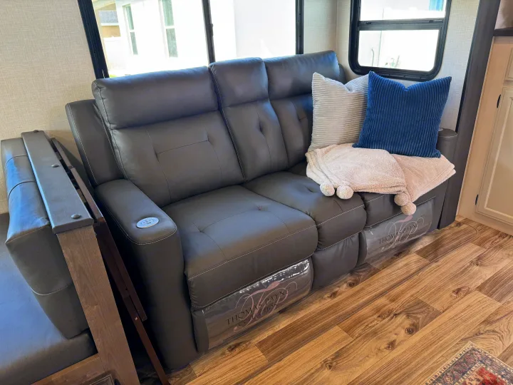 Comfortable gray reclining sofa with pillows & blanket in a modern RV interior for your RV rental.. SportTrek Venture 2024