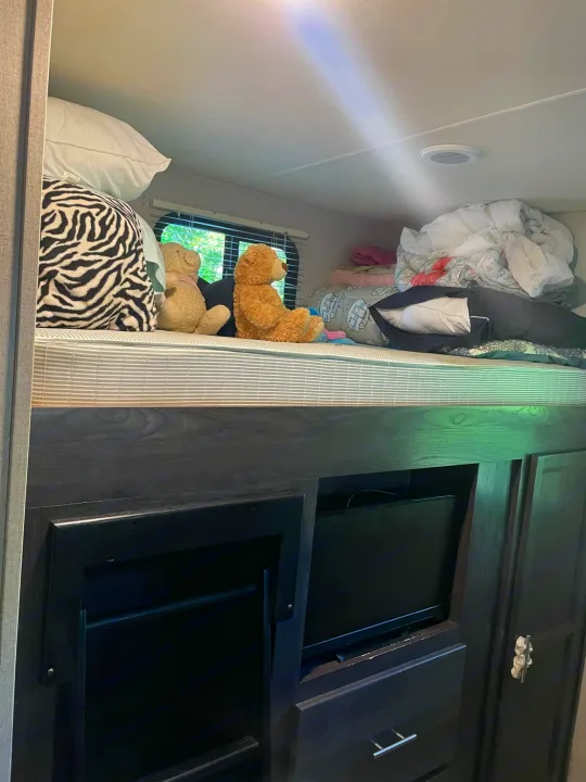 RV rental interior: A cozy bunk bed with soft bedding and teddy bears. Below, dark cabinets offer entertainment & storage.. Dutchmen Kodiak Ultra-Light 2018