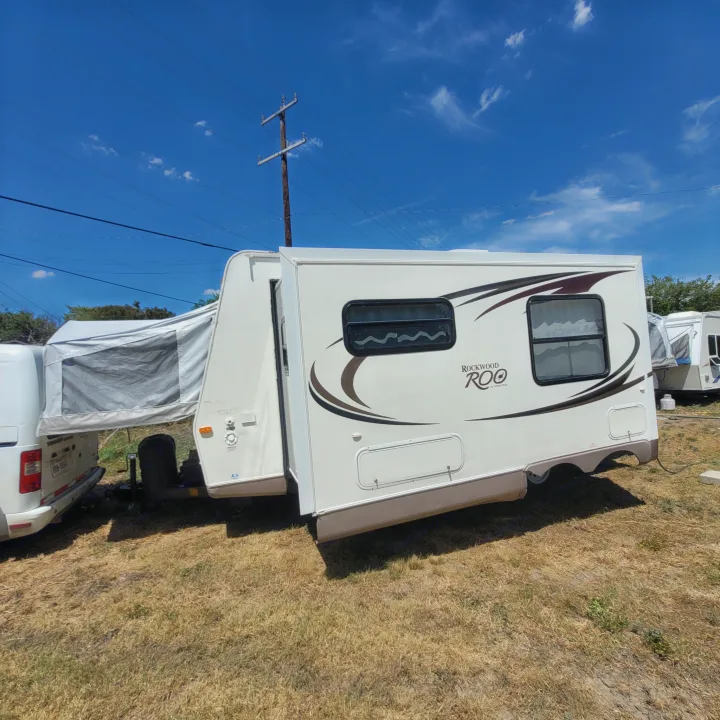 A white Rockwood Roo hybrid travel trailer RV rental, featuring an expandable tent, parked on dry grass.. Forest River Rockwood Roo 2011
