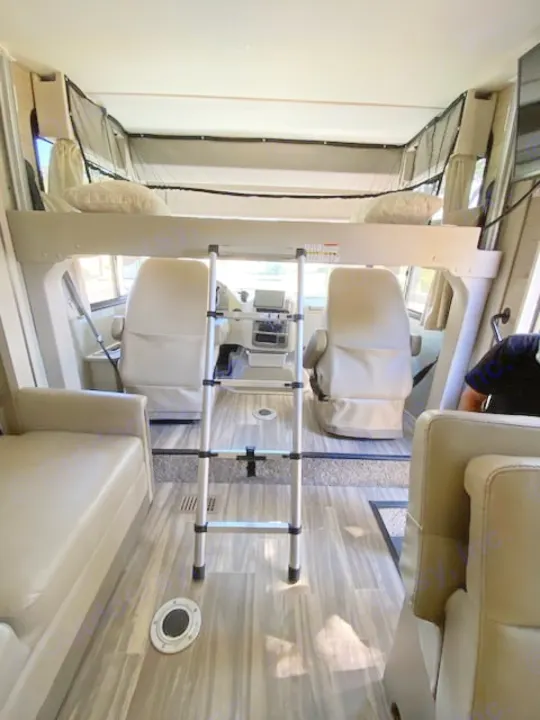RV rental interior: Overhead bunk with ladder over driver/passenger seats, plus a side couch.. Thor Axis 2023