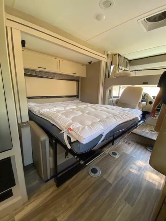 Explore this RV rental's cozy interior, featuring a lowered drop-down bed, overhead cabinets, and durable flooring.. Thor Axis 2023