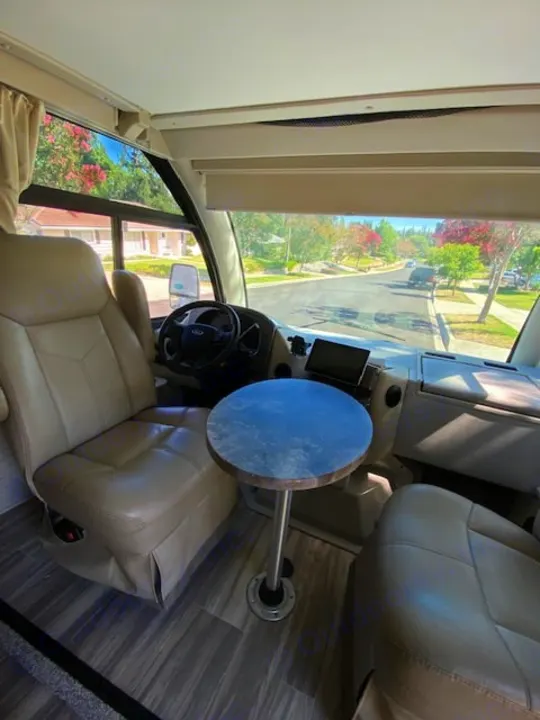 RV rental cab view: Spacious front seats, small table, and a clear street view through the windshield.. Thor Axis 2023