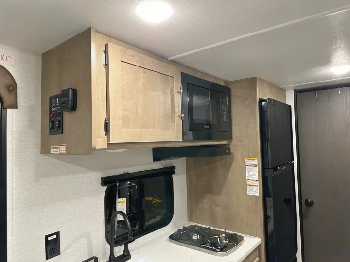 Experience RV rental comfort: A compact kitchen featuring a microwave, two-burner stove, refrigerator, sink, and overhead cabinets.. Keystone RV Springdale Mini 2025