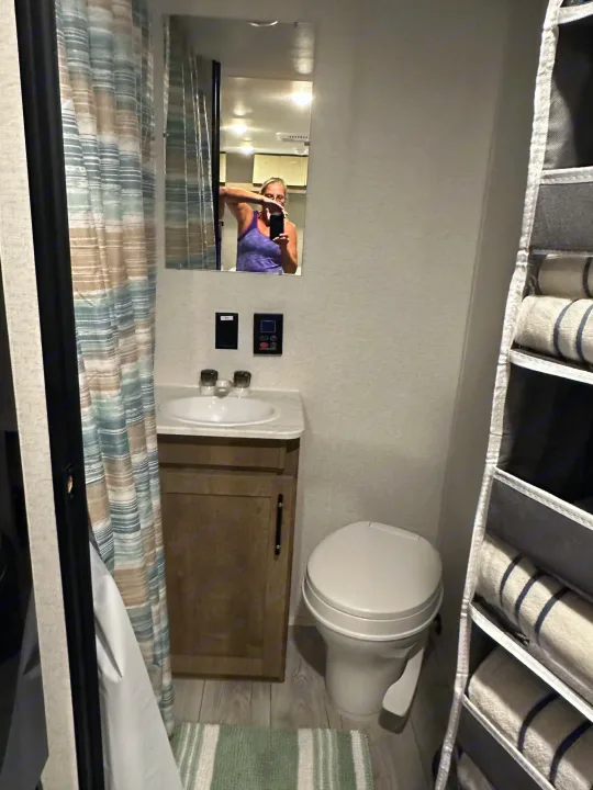 RV rental's compact bathroom features a sink, toilet, shower, and hanging towel storage, demonstrating efficient space.. Keystone RV Springdale Mini 2025