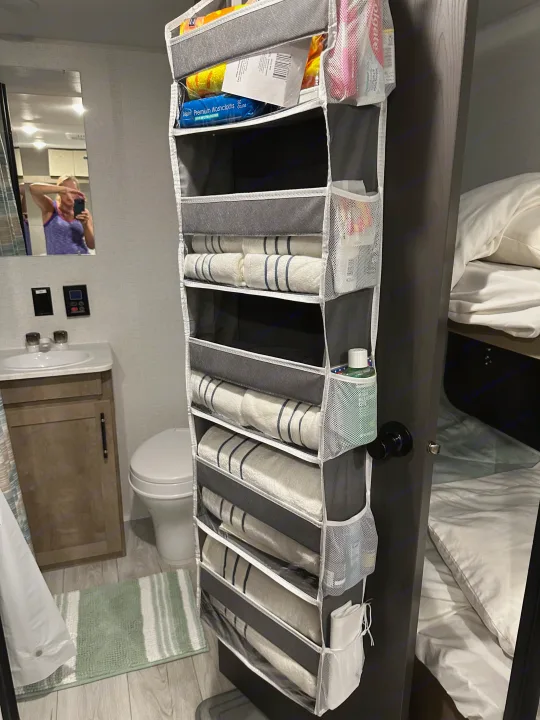 RV rental bathroom features a sink, toilet, mirror, and efficient hanging organizer with towels/toiletries, next to a bunk.. Keystone RV Springdale Mini 2025
