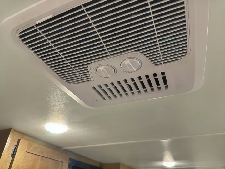 White Furrion RV air conditioner with fan & temperature controls mounted on a textured ceiling in an rv rental.. Keystone RV Springdale Mini 2025