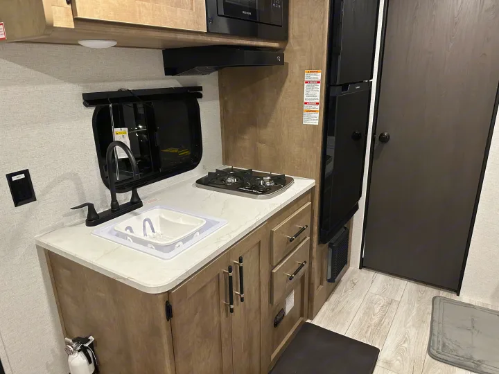 Well-equipped compact kitchen in an RV rental, featuring a sink, stovetop, microwave, and refrigerator for easy travel cooking.. Keystone RV Springdale Mini 2025