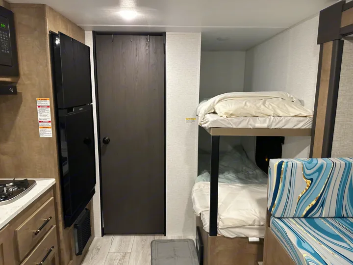 Modern RV rental interior with kitchen, black fridge, door, cozy bunk beds, and a patterned cushion.. Keystone RV Springdale Mini 2025