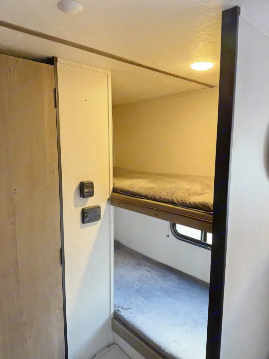 RV rental bunk beds: a cozy, compact sleeping area with essential controls and a window. Perfect for family trips.. Keystone RV Springdale 2022