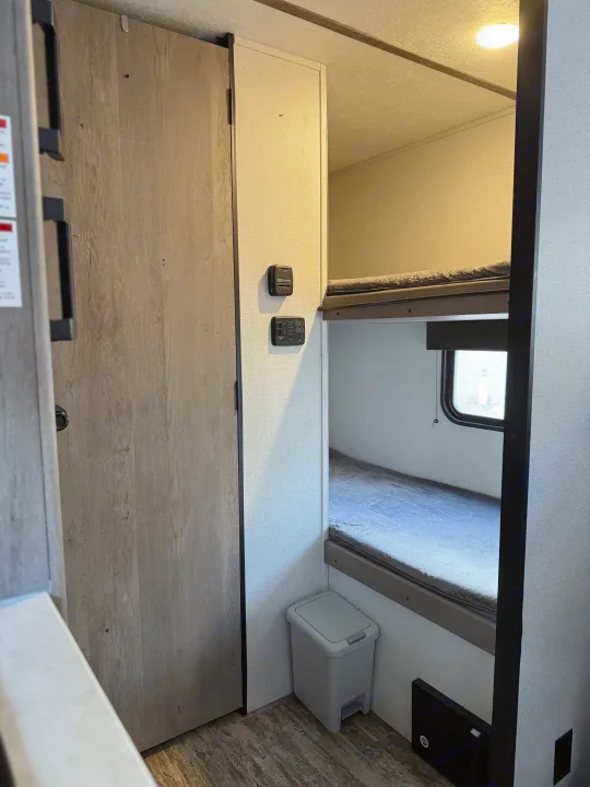 Step into this RV rental, revealing a smart interior with bunk beds, a closet, and wall-mounted controls, designed for efficient living.. Keystone RV Springdale 2022