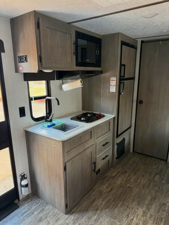 Compact RV rental kitchen interior features sink, stove, microwave, and fridge, maximizing space.. Keystone RV Springdale 2022