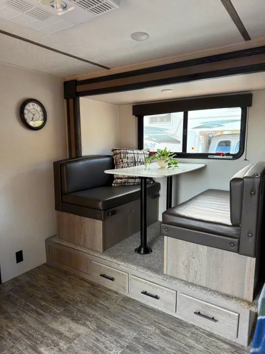 Inside an RV rental: a modern dinette with dark leather-like booth seating, light wood bases, and storage drawers.. Keystone RV Springdale 2022