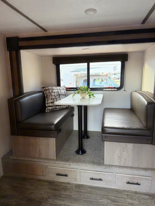 View of an RV rental dinette featuring black cushioned benches, white table, window, and lower storage drawers.. Keystone RV Springdale 2022