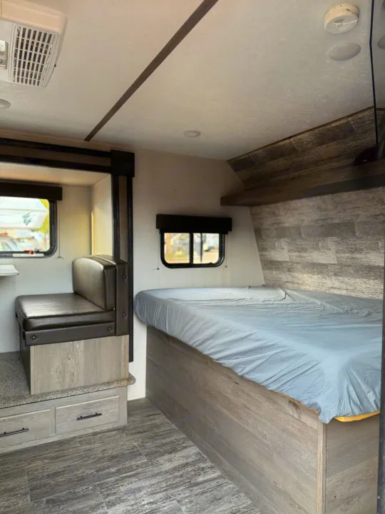 RV rental interior: A modern space featuring a cozy bed, dining area with storage, and stylish wood-look details.. Keystone RV Springdale 2022