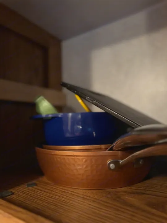 Inside an RV rental cupboard: stacked copper pan, blue bowl, and lid. Compact kitchen storage for travel.. Forest River Wildwood 2000