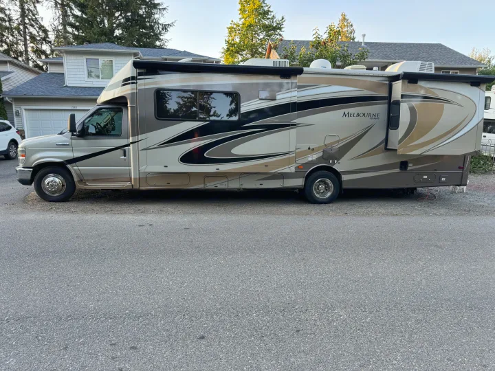 A large, beige Class C Jayco Melbourne motorhome RV rental is parked on a residential street with a house in the background.. Jayco Melbourne 2012