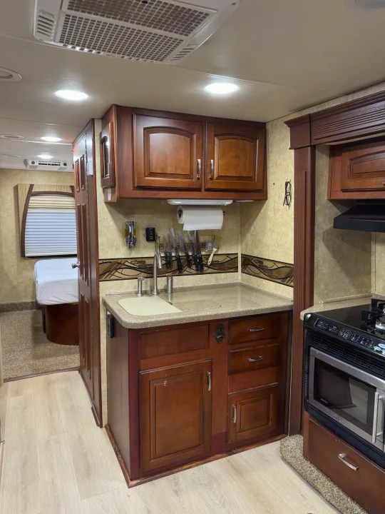 RV rental interior features a kitchen with sink, stove, microwave, wood cabinets, and glimpse of bedroom.. Jayco Melbourne 2012