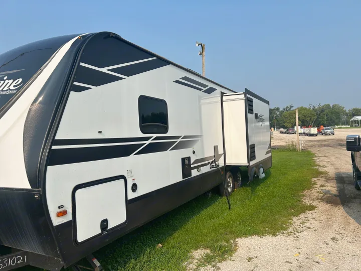 Spacious white and black RV rental parked on grass, featuring an extended slide-out for extra room.. Grand Design Imagine 2021