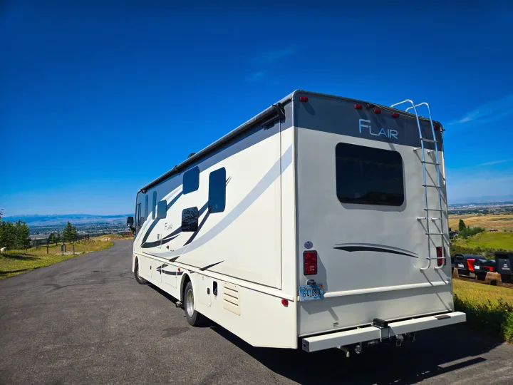 An RV rental parked on a scenic overlook, offering a great view of the valley and mountains under a clear blue sky.. Flair-Fleetwood Flair-Fleetwood Motorhome 2019