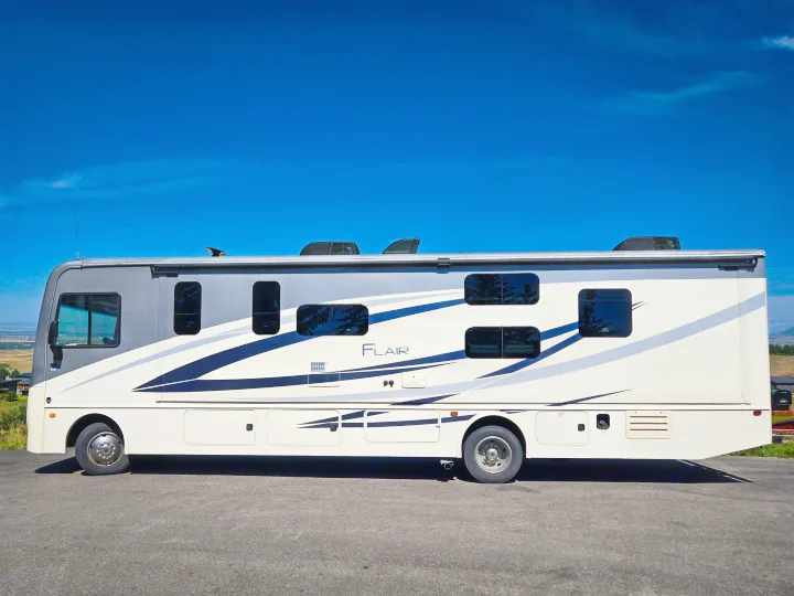 Side view of a grey and white Flair recreational vehicle, perfect for an rv rental, parked under a clear blue sky.. Flair-Fleetwood Flair-Fleetwood Motorhome 2019