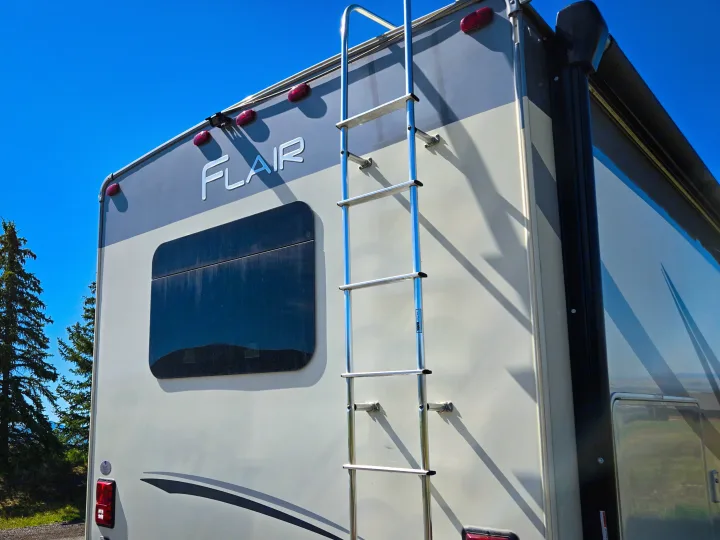 Rear view of an RV rental, featuring a ladder, window, and awning, set against a clear blue sky.. Flair-Fleetwood Flair-Fleetwood Motorhome 2019