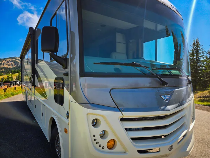 Experience the open road with an RV rental! This sleek motorhome is parked on a sunny day amidst scenic mountains and nature.. Flair-Fleetwood Flair-Fleetwood Motorhome 2019