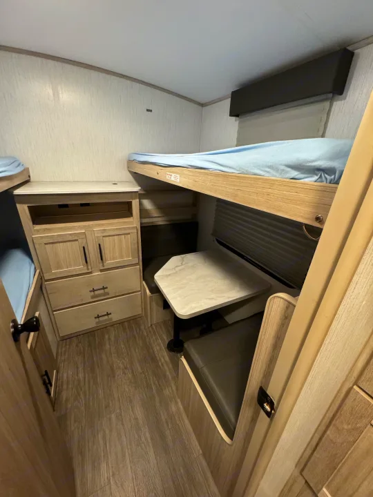 Interior of an RV rental: light wood-paneled bunk beds, dinette table, and storage cabinets on wood-look flooring.. Cruiser RV Shadow Cruiser 2022